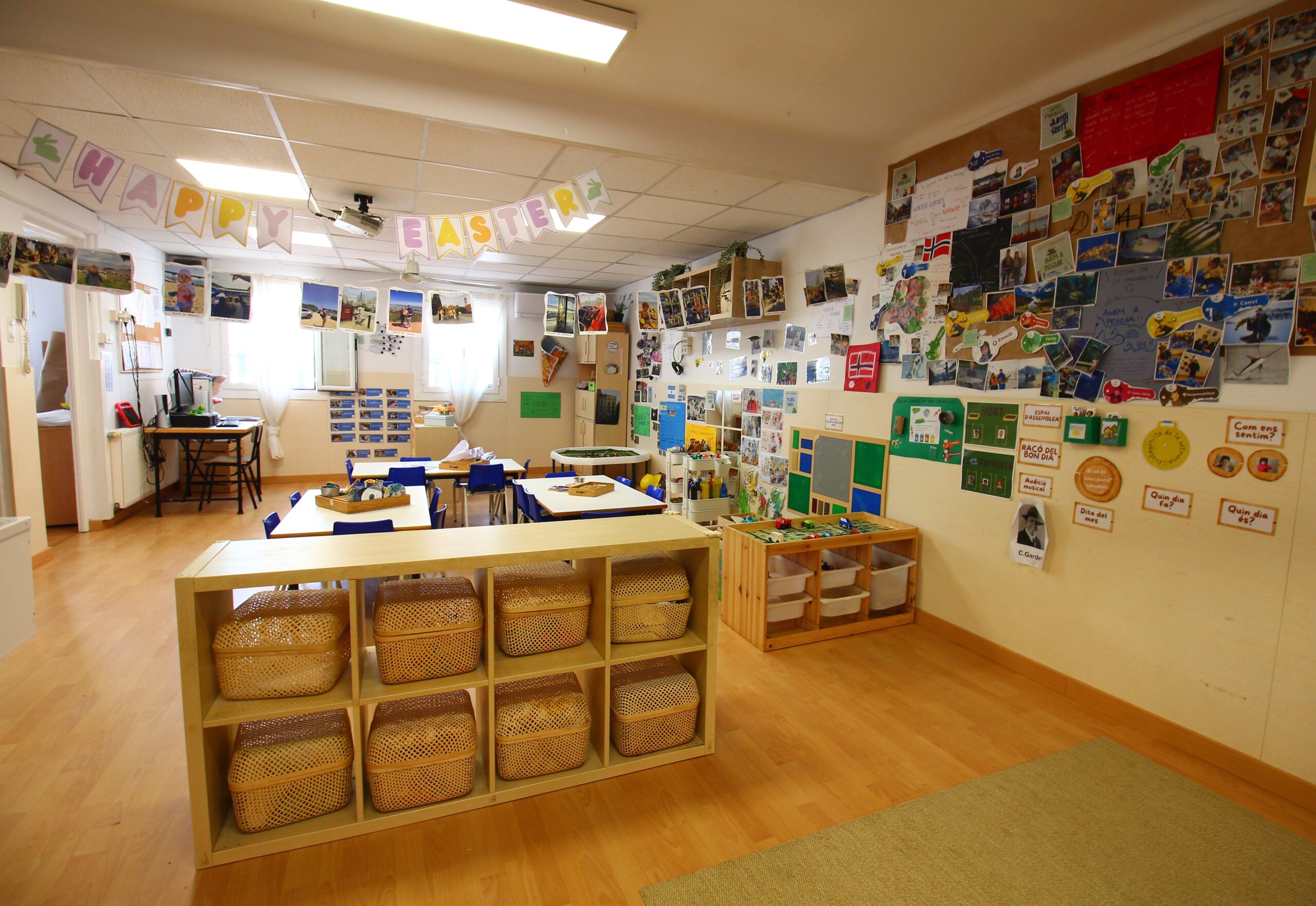 Aula amb taules, prestatgeries i cistells de materials